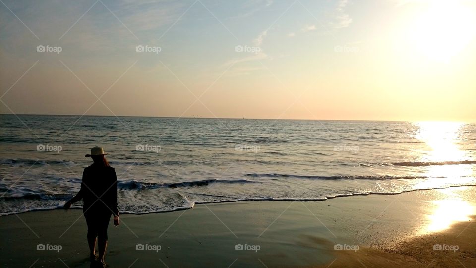 Beach at sunset with sillohuete of woman walking.