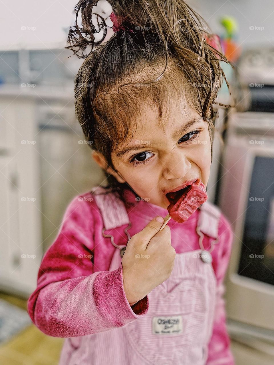 Toddler girl eats Popsicle, toddler girl with funny expression eating delicious dessert, toddler enjoys a treat, eating a Popsicle with tenacity, toddler girl loves popsicles, eating a raspberry fruit popsicle 