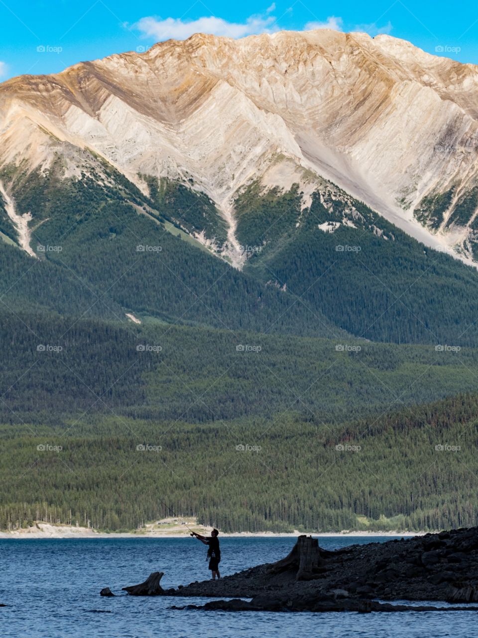 Fisherman Casting into a Blue Lake, with a Mountain Background, in Kananaskis.