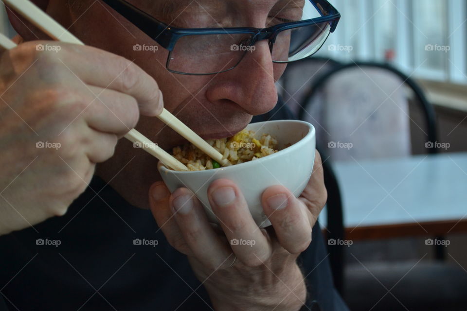 Caucasian man eating Chinese food from bowl with chopsticks 