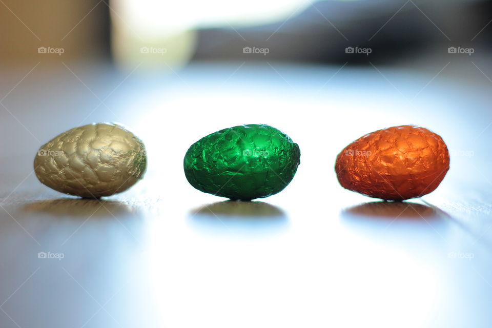 A portrait of three chocolate easter eggs wrapped in colorful tin foil on the floor. the shallow depth of field gives the photo another dimension.