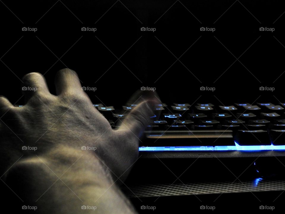 Teenager boy playing Minecraft on the gaming computer seen from his left side and close-up of his hand playing in a dark room.