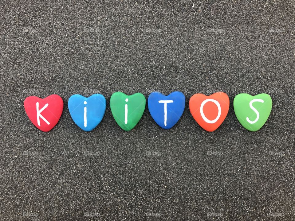 Kiitos, finnish thank you with colored heart stones over black volcanic sand