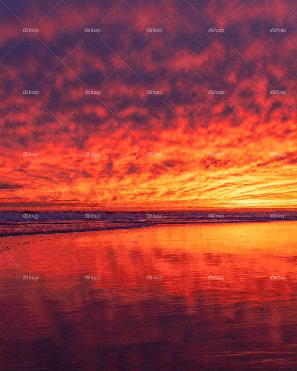 Vibrant colorful sunset clouds reflecting on the wet sand of a beach with waves crashing the background