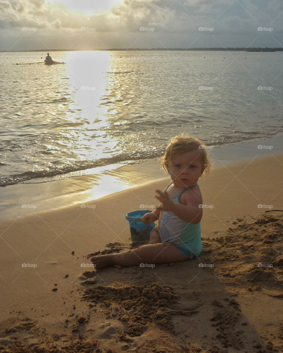 baby sitting on coast at sunset