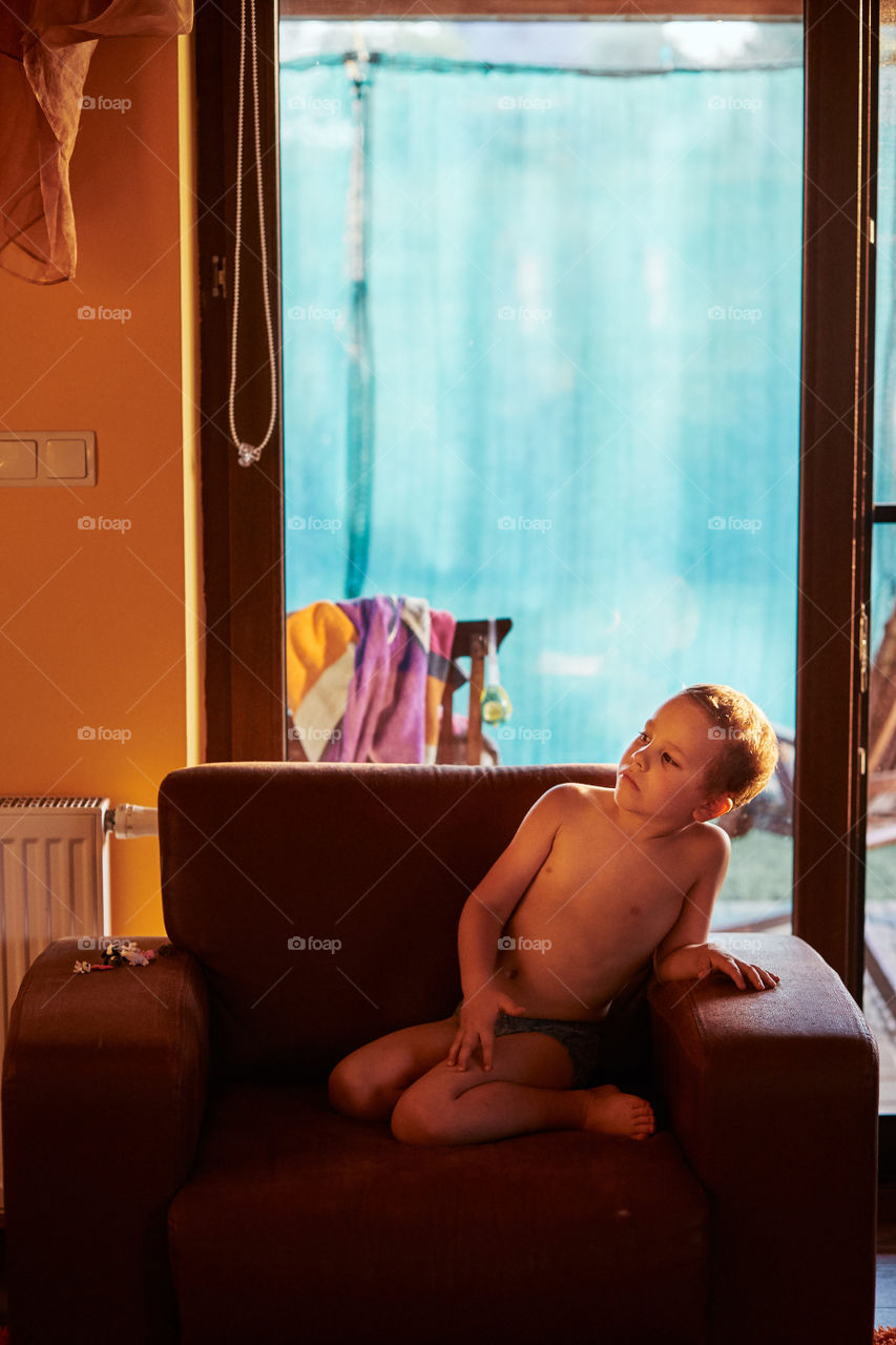 Little boy watching a movie sitting in a armchair at home. Candid people, real moments, authentic situations
