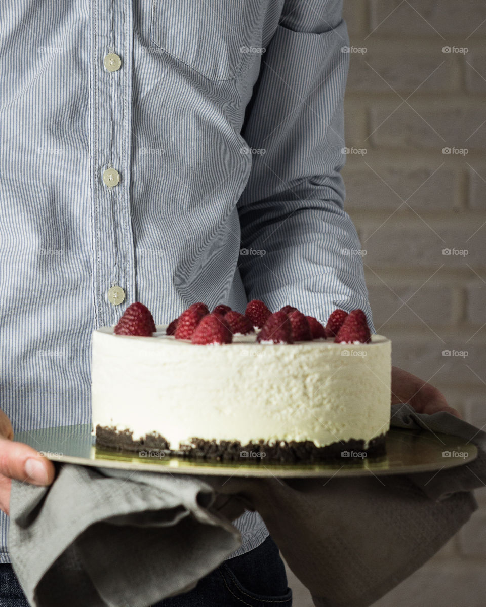 Man is holding delicious raspberry cheesecake.