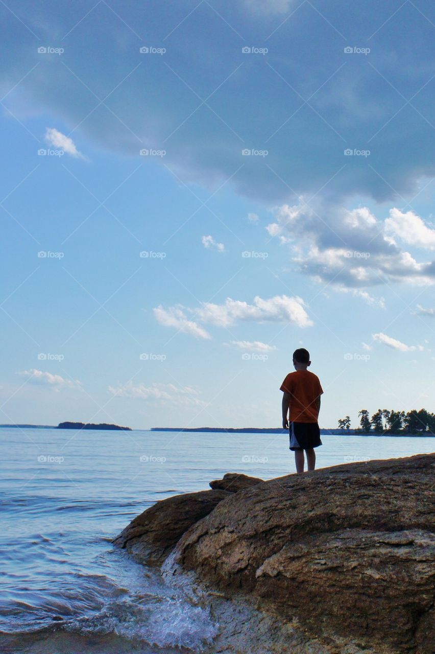 Rear view of boy standing at lakeshore