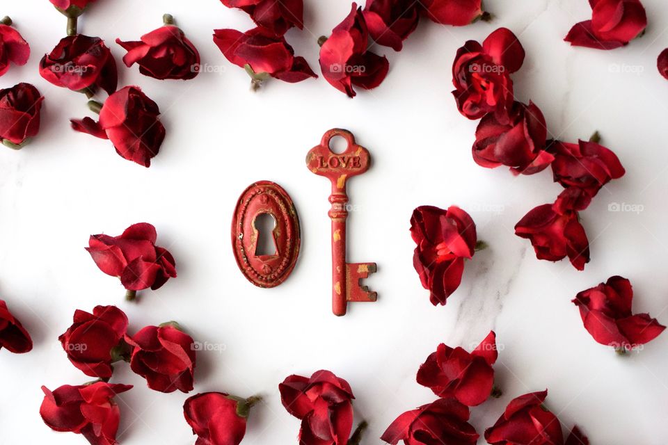 Red, metal, vintage key and keyhole with red, silk rose buds on white marble surface