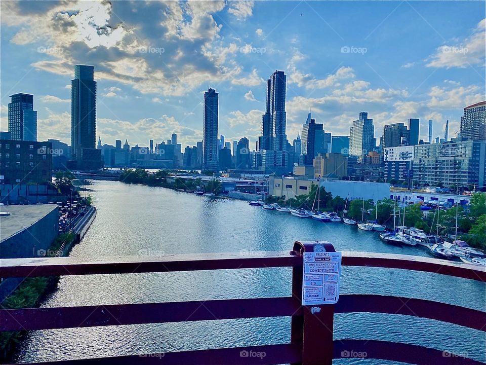 A panoramic view over the “E River” at “Newtown Creek” photographed from atop the “Pulaski Bridge” at the “Greenpoint, Bklyn” side. Far away the “Manhattan skyline” and the outlines of “LIC, Queens” buildings can be seen. 2022. Hypnotic Productions