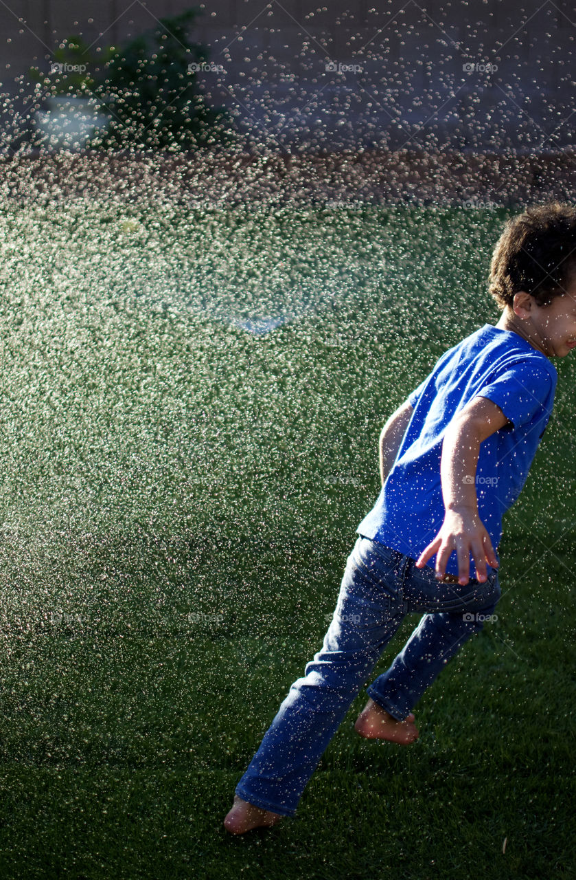 Boy running outside in sprinklers 