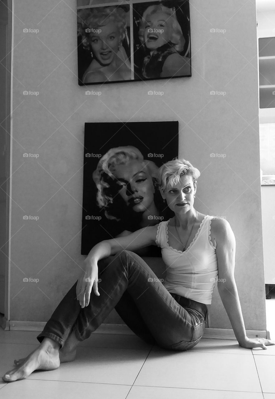 Black and white portrait of a woman in her apartments, on the background of photographs of actress Marilyn Monroe