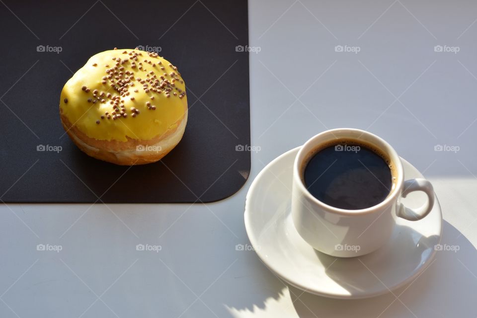 cup of coffee and bun sweet in sunlight on a white and brown background, morning routine