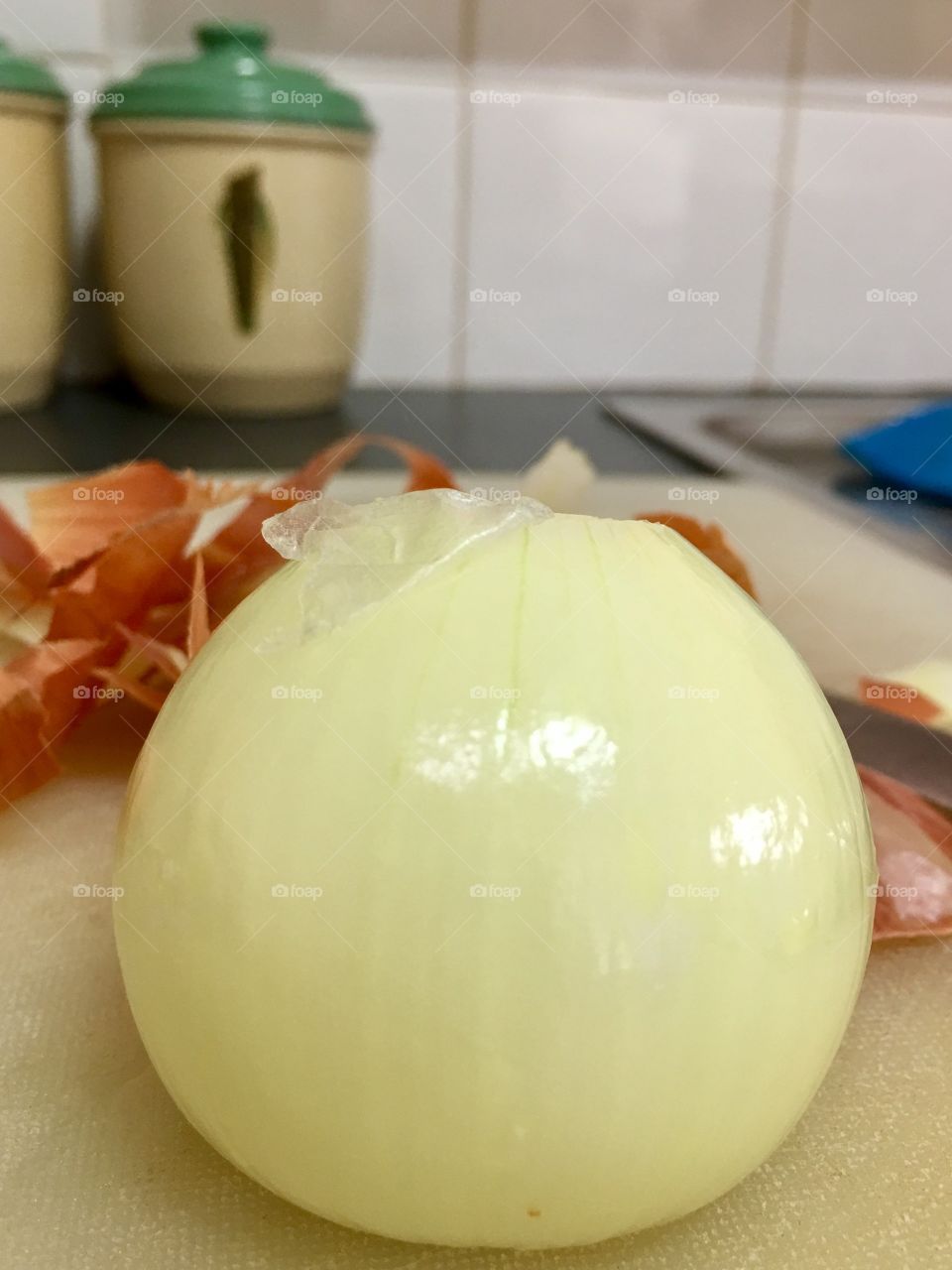 Single white peeled onion closeup, skin and knife in background, food prep