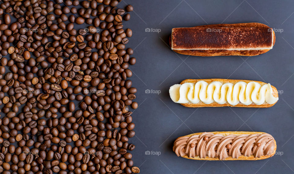 Three desserts eclairs near the coffee beans. Top view.