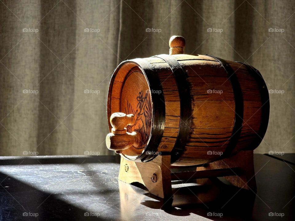 Old beer barrel on a dark table illuminated by the sunlight passing through the window.