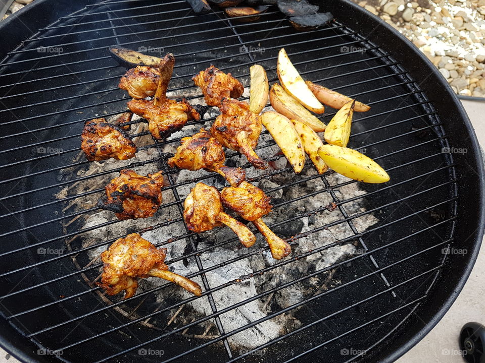 Cooking potato wedges and marinated chicken pieces on a BBQ