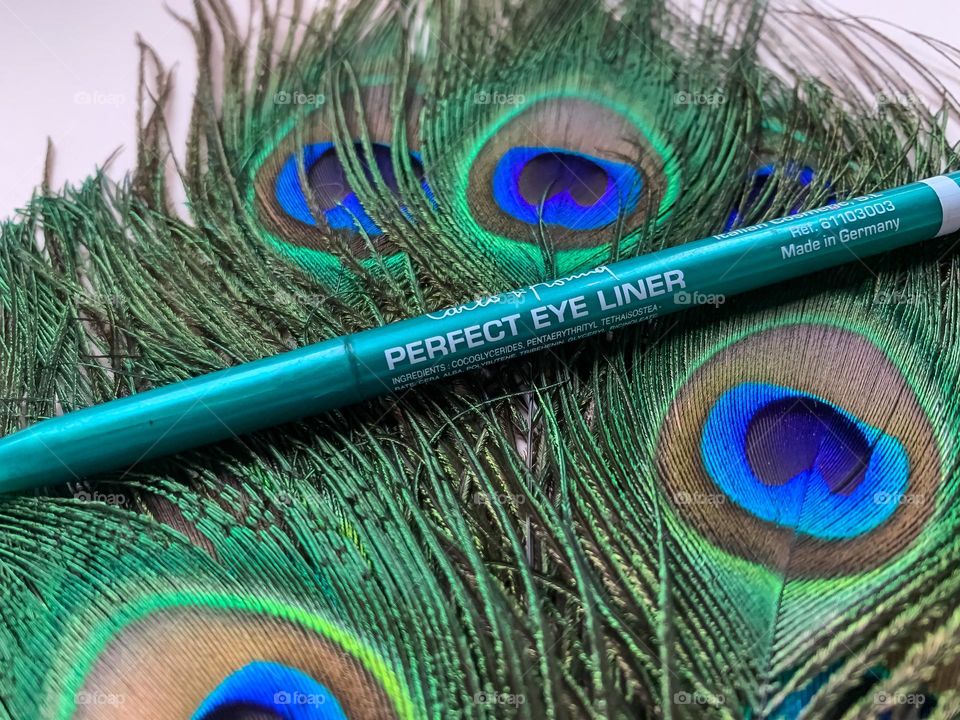 Green eyeliner displayed on a bed on peacock feathers