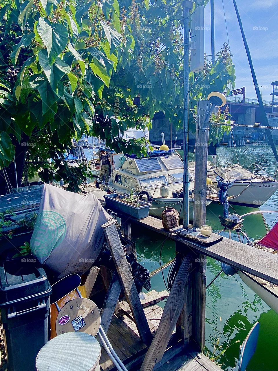 This is a wonderful view of the boats tied to the LIC shore  at “Newtown Creek” by the “Pulaski Bridge” seen from the handmade wooden porch that is sometimes used for parties and get togethers. 2023. Hypnotic Productions