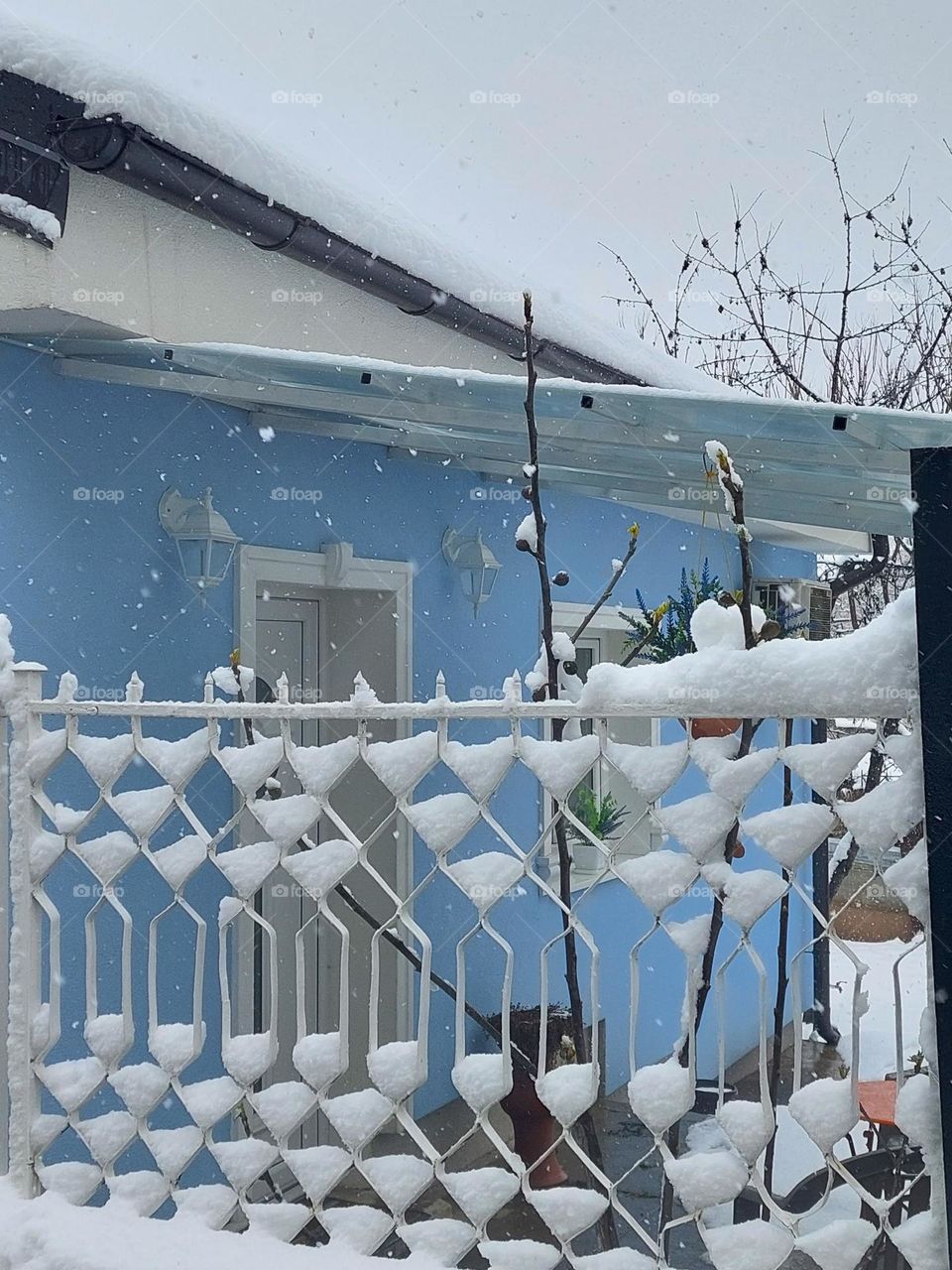 Blue-white Winter idyll.  Blue house with white details and fence decorated with falling snow