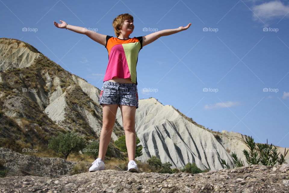 The model is on a rock. Behind you can see mountains and trees. A beautiful landscape The landscape looks like a desert landscape but it is a place where there is countryside.