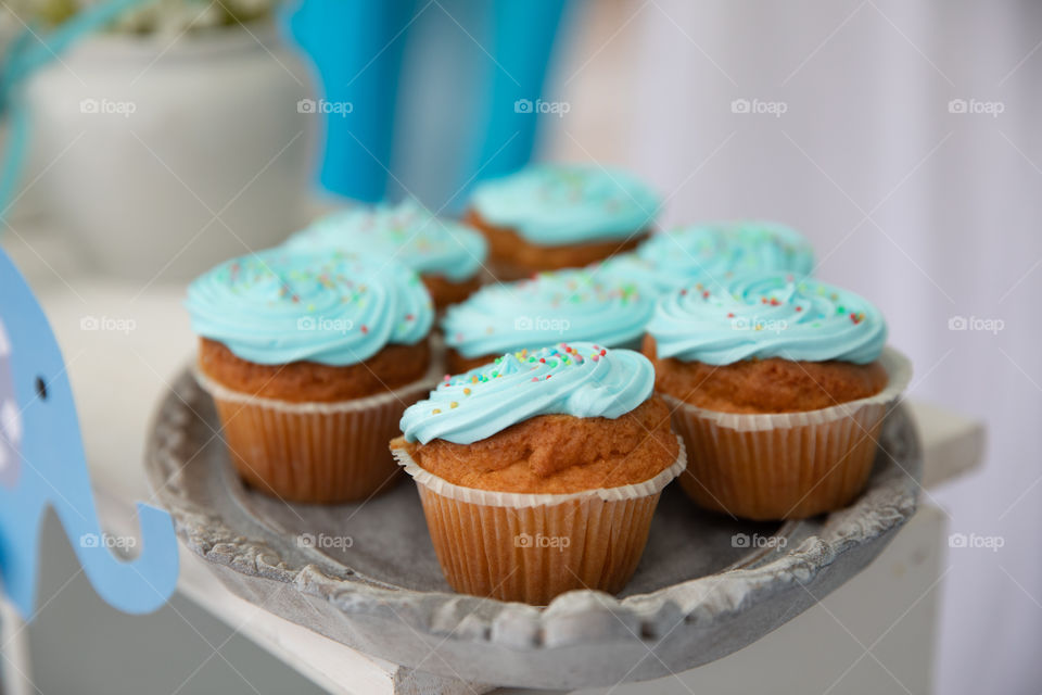 Tasty handmade freshly baked muffins with cream and colorful toppings, arranged on tray.