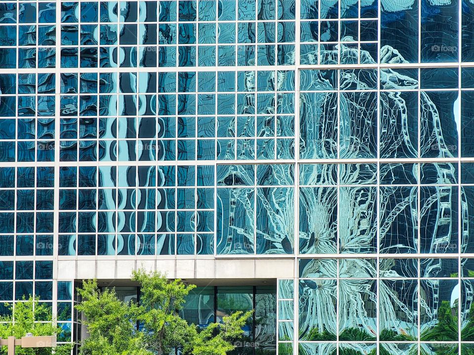A Ferris Wheel is reflected in a downtown glass building in a major metropolitan area