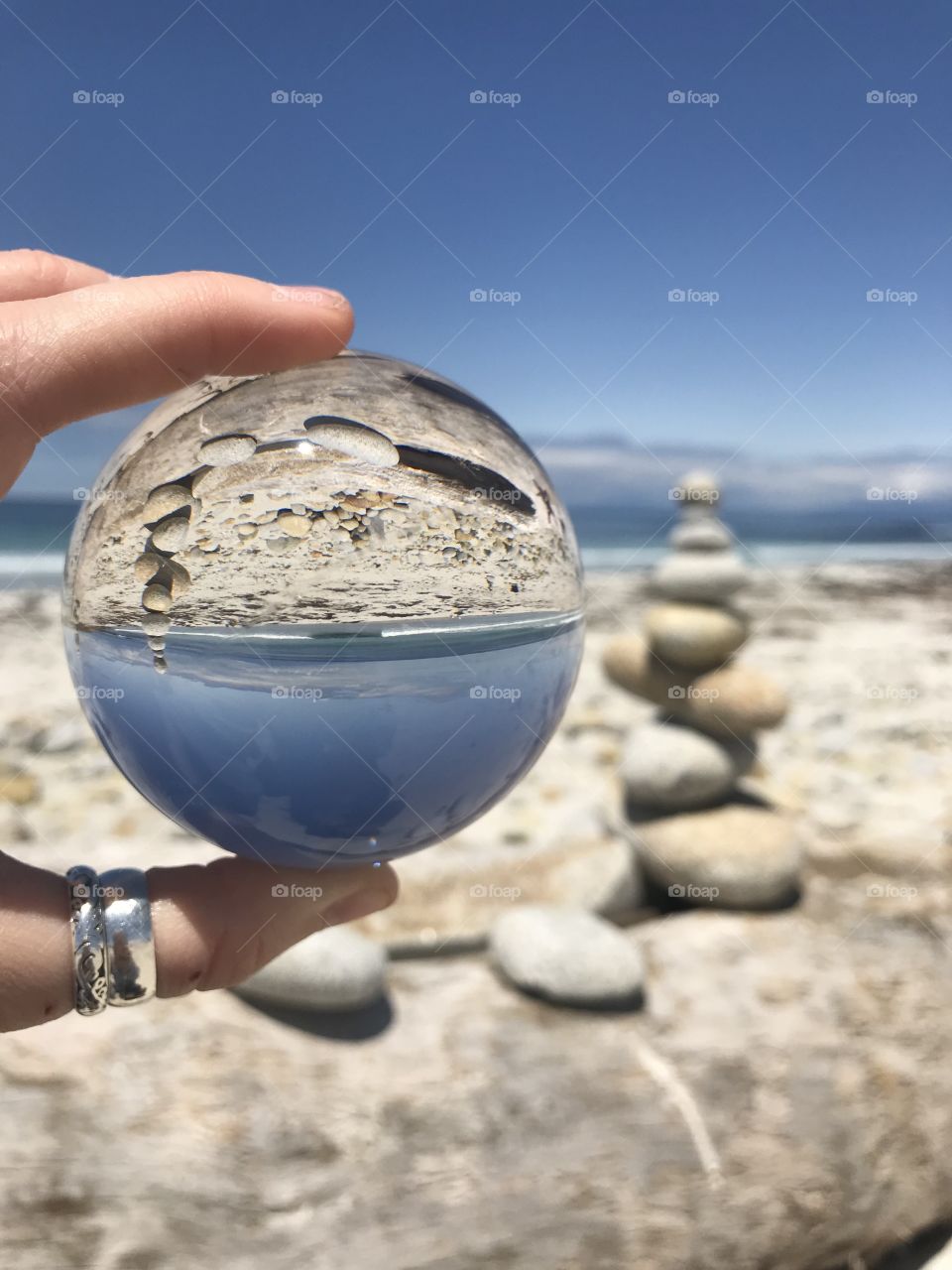 An image of a man-made stack of beach stones on the shoreline flipped upside down by a crystal ball. 