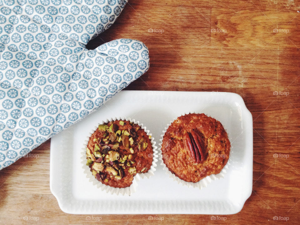 Two healthy breakfast muffins with nuts on a white plate on top of a wooden counter and a blue and white ovenglove next to it.