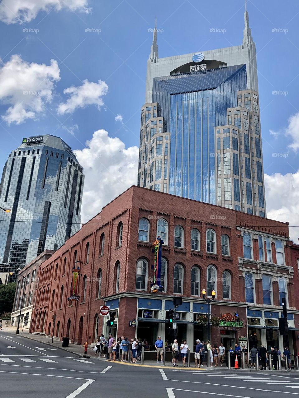 Queue crowd lining up to get into Margaritaville bar in downtown Nashville Tennessee in front of Batman AT&T building mirror clouds sky sunny summer day skyscrapers city skyline 