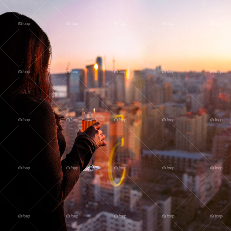 Woman holding wine glass at sunset city view