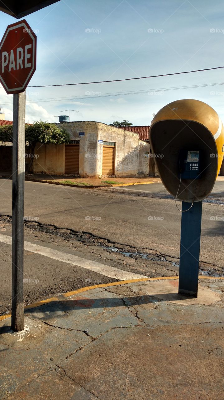 Esquina, rua, placa de trânsito PARE, velho salão e um orelhão.
