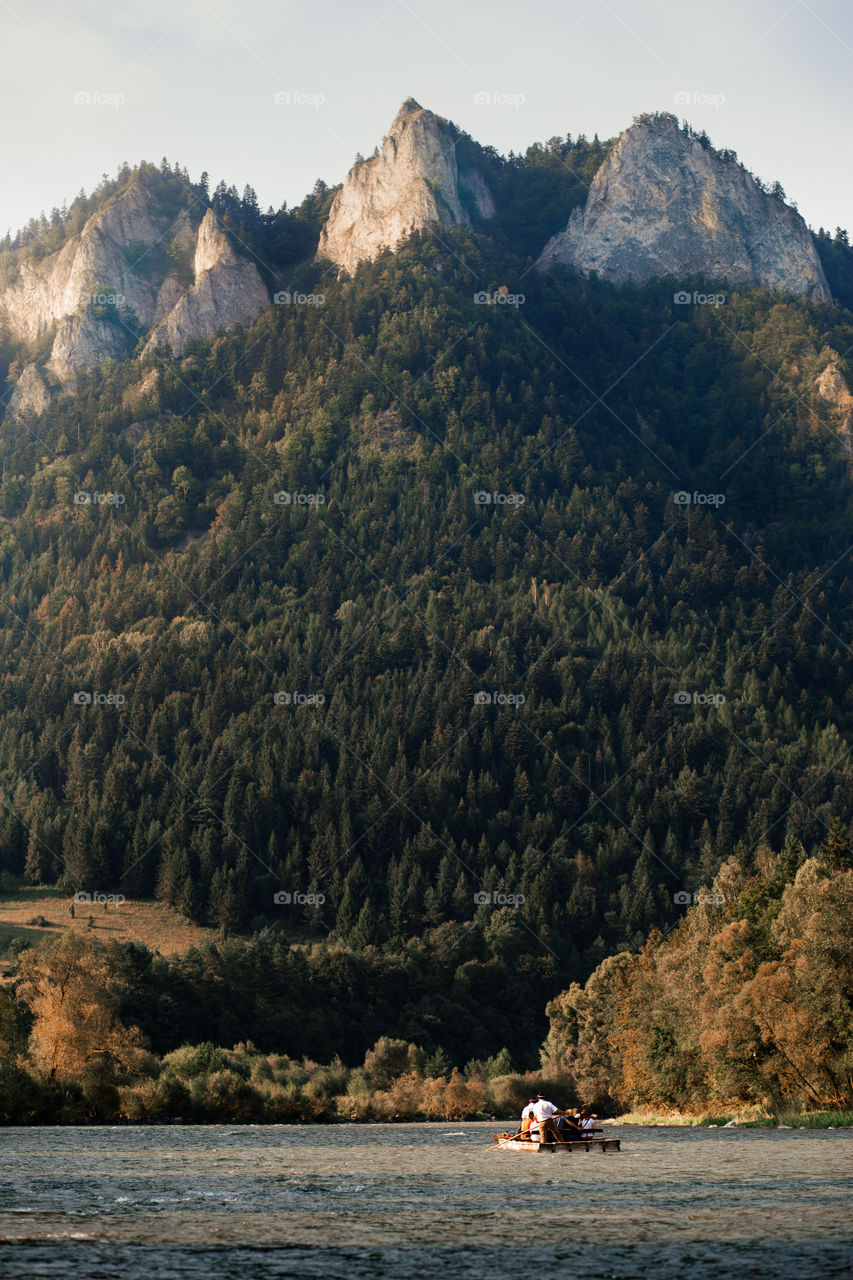 Raft ride on The Dunajec river at the foot of  Pieniny Mountains. Group of people enjoying trip on raft going down the river. Trzy Korony (Three Crowns) peak over the river