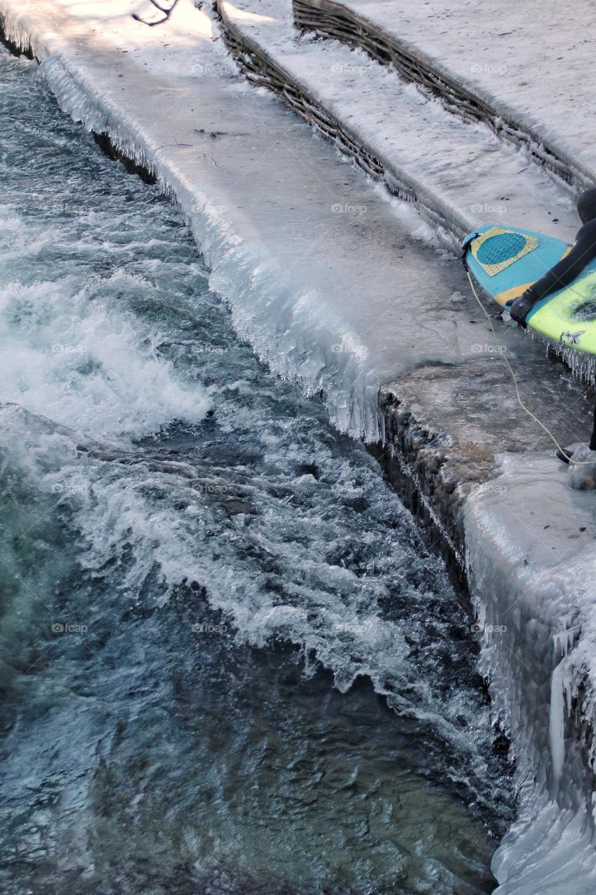 Stairs covered with ice and icicles on the stream and a surfer with a surfboard 