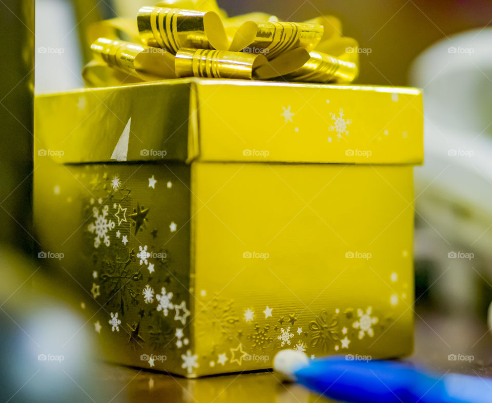 A bright yellow golden box with a bow asterisks with a Christmas present is standing on a brown table.