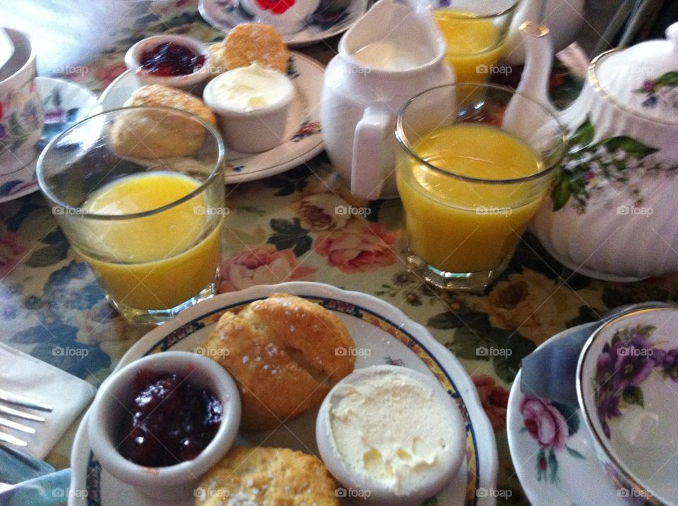 Homey British breakfast of biscuits, muffins, jam, clotted cream with tea and orange juice on finely set table 
