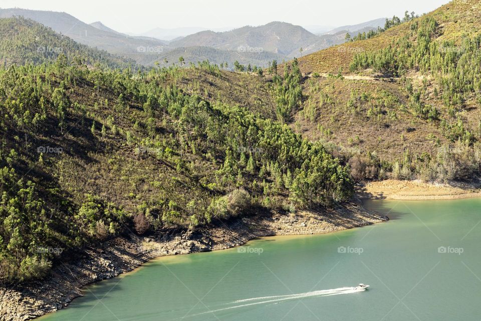 A speedboats travels along the Rio Zêzere as mountains reach off into the distance