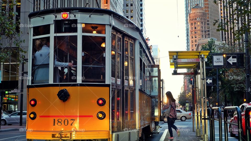 A yellow trolley in San Francisco picking up a passenger. 