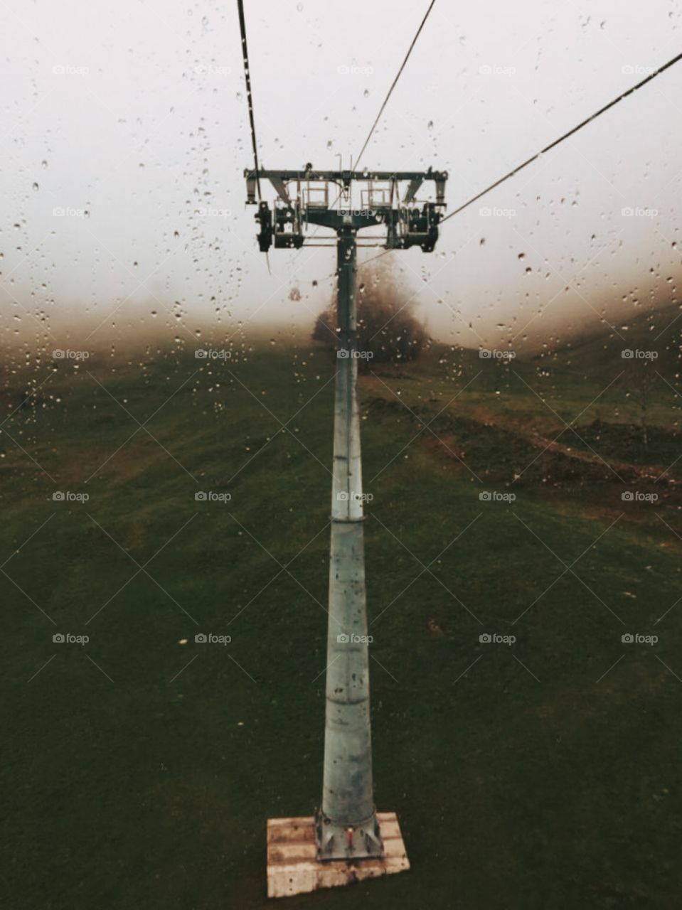 A pillar with three cables . Water droplets on the glass frame . view while sitting on the cable car . raining and foggy in the mountain .