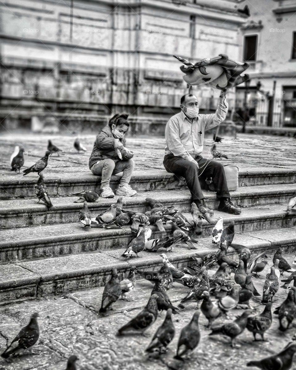Man holds balloon, while child feeds the birds