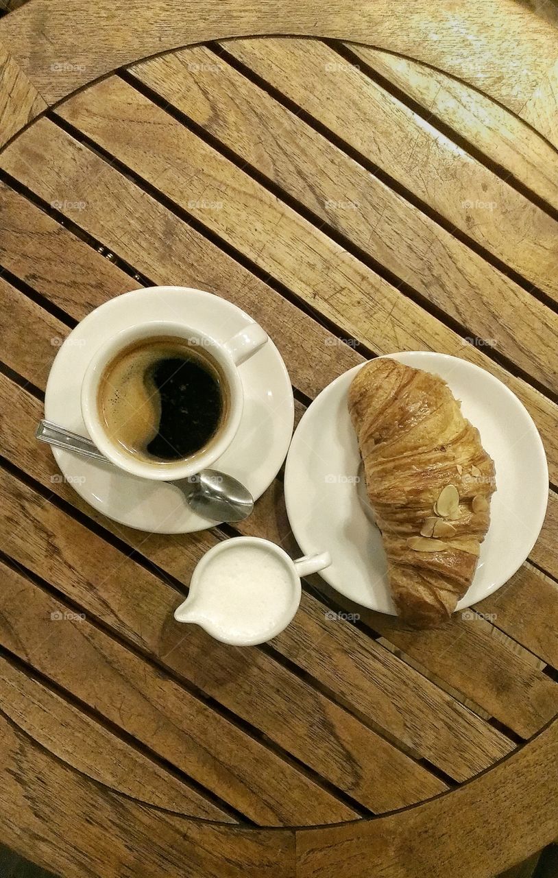 A cup of coffee with croissant on wooden table