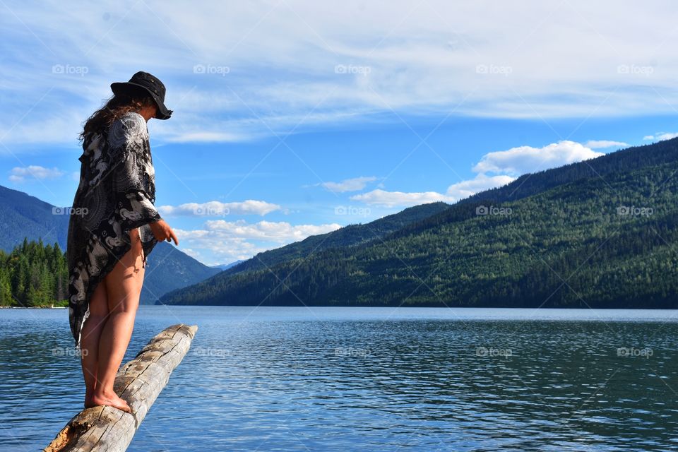 A majestic, beautiful, woman balancing on a log teetering over a lake in Revelstoke, BC 