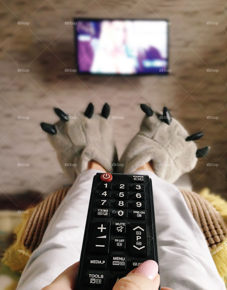 Watching television in cozy bed wearing funny home slippers 