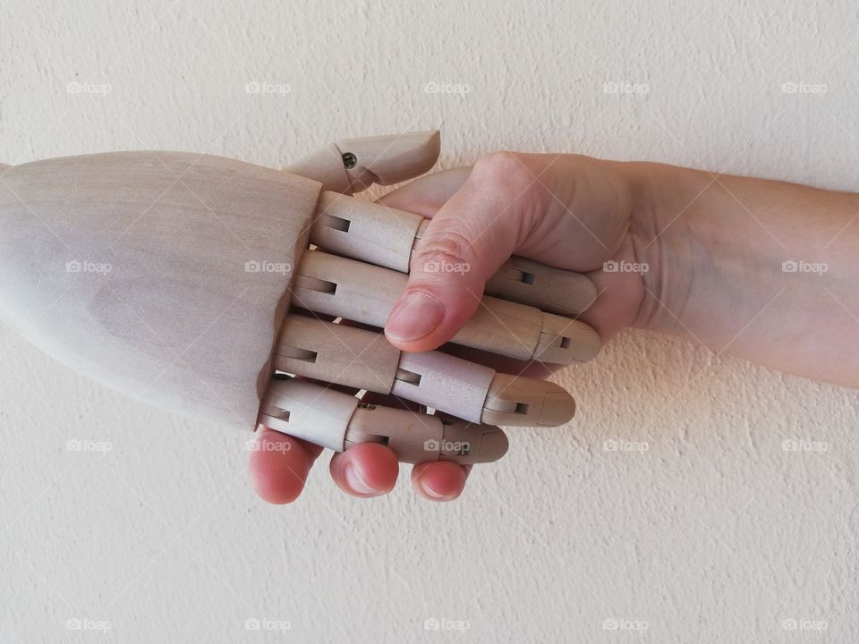 Wooden hand shakes the hand of a human being