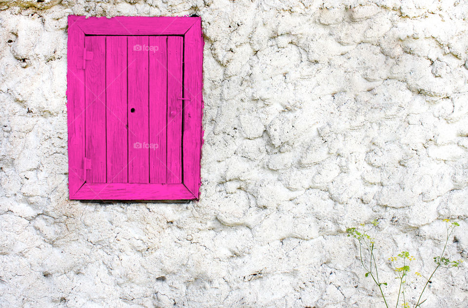 Pink painted wooden window on white wall, exterior