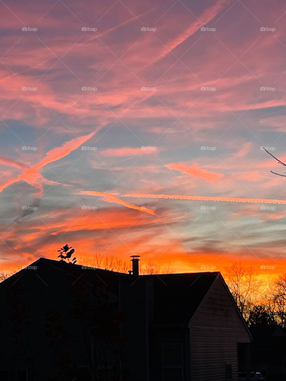 Pastel colored sunset with streaks in the sky and a silhouette of a house 