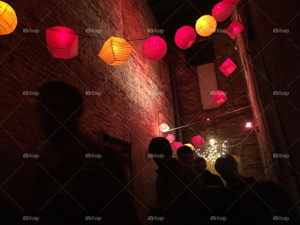 Silhouetted people walking under colorful hanging lanterns in a narrow alley