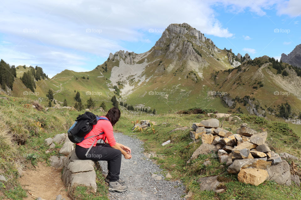 Female hiker resting on rock in front of mountain scenery.