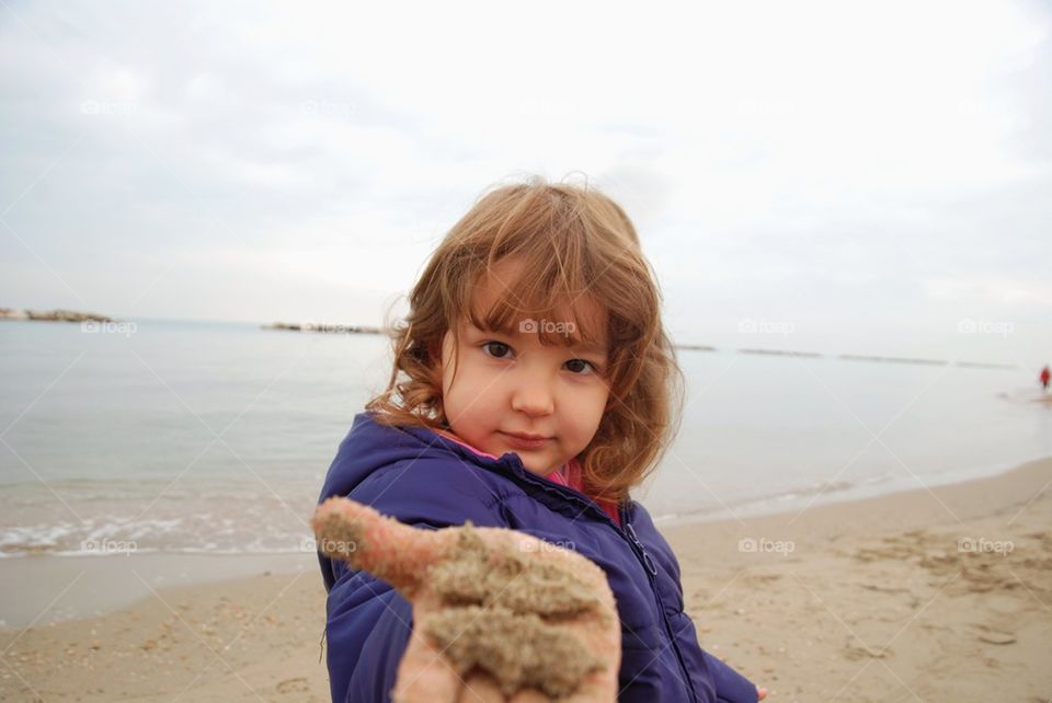 Baby girl with wet sand on her palm hand