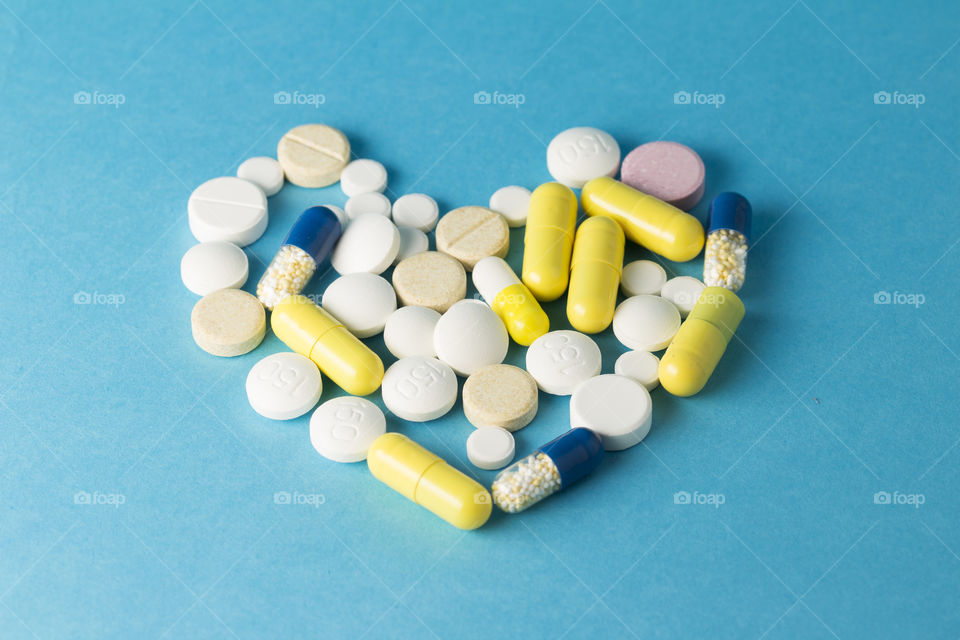 Medicines white,yellow, blue round heart shaped pills on blue background